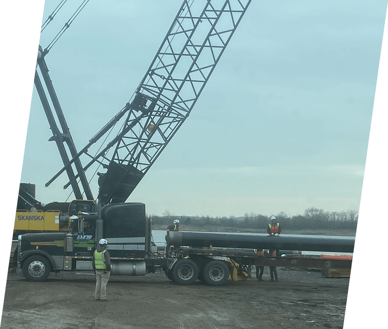 A large crane is lifting a pipe from the ground.